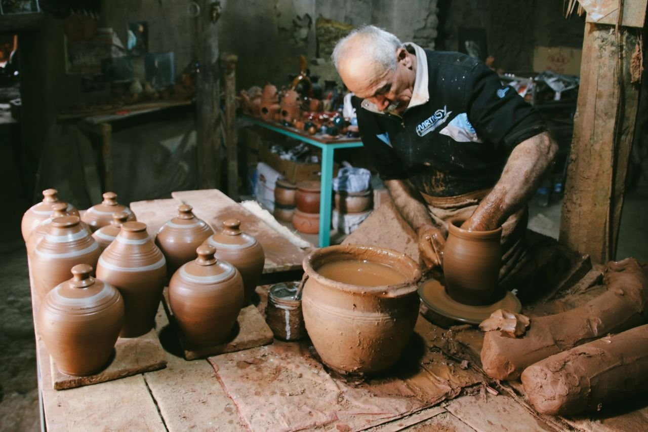 Senior man handcrafting pottery jugs in a traditional workshop, showcasing skilled craftsmanship.